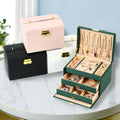 Green jewellery box open with drawers, with pink, white and black boxes behind; jewellery shown for styling