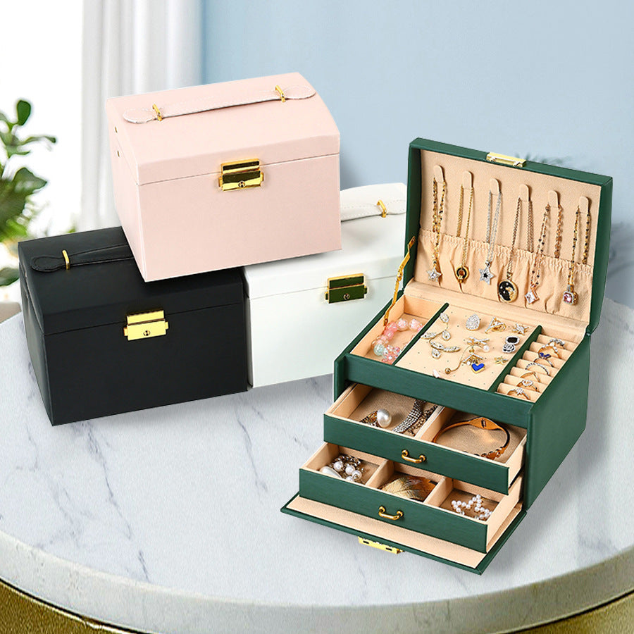 Green jewellery box open with drawers, with pink, white and black boxes behind; jewellery shown for styling